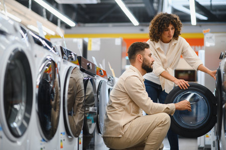 Young couple browsing through a variety of washing machines in an appliance store, making thoughtful decisions for their home laundry needsの写真素材