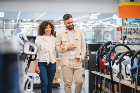 Happy couple walking arm in arm through a spacious electronics store, discussing options while choosing a new vacuum cleaner togetherの写真素材