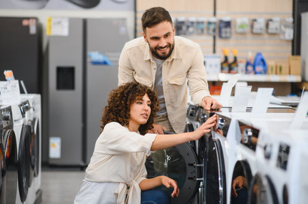 Happy couple selecting new washing machine in a home appliance store, making purchasing decisions together for their householdの写真素材