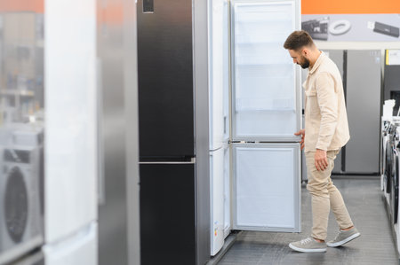Man opening refrigerator door, examining features in home appliance store, making purchase decision for kitchen upgradeの写真素材