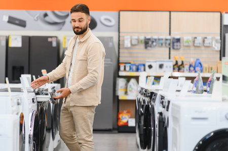 Bearded man selecting new washing machine in appliance store, comparing features and models before making purchaseの写真素材