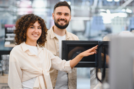 Happy couple selecting new microwave oven in a home appliance store, making purchasing decision for their kitchenの写真素材