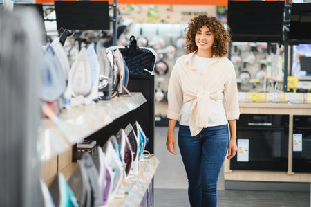 Smiling woman walking through electronics store, choosing new iron among various models, shopping for home appliancesの写真素材