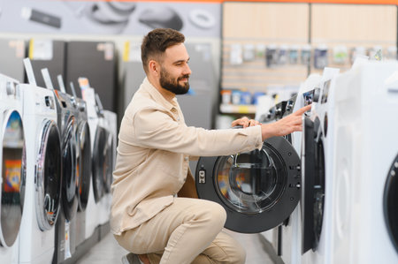 Bearded man selecting new washing machine in appliance store, examining features and making purchase decisionの写真素材