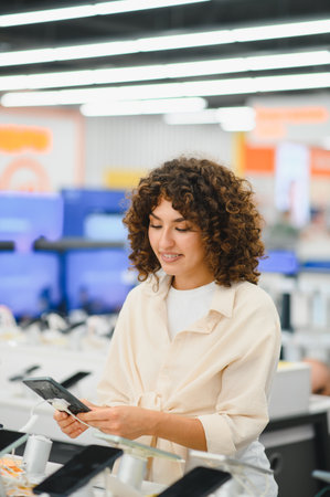 Smiling woman with curly hair browsing and comparing new mobile phones in a vibrant consumer...