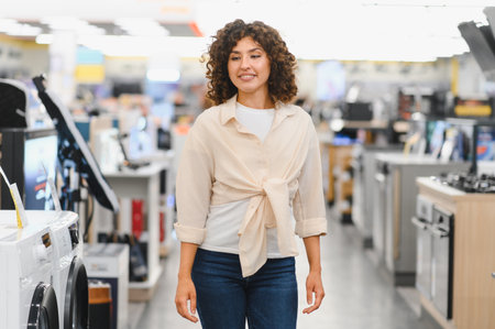 Young woman walking through electronics store, looking at various home appliances and deciding what...