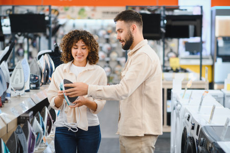 Young couple choosing a new iron in an electronics store, the woman holding a new appliance while...