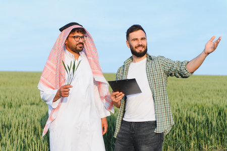 Agronomist with clipboard showing wheat field to arab businessman holding spikelets in his hand