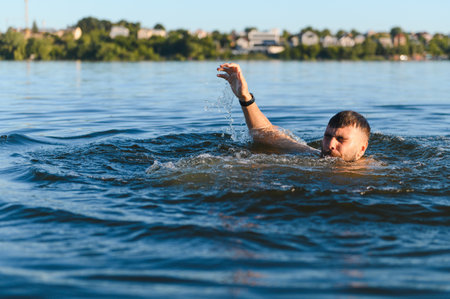 Desperate man struggles in a lake, raising a hand for help while gasping for breath, surrounded by...