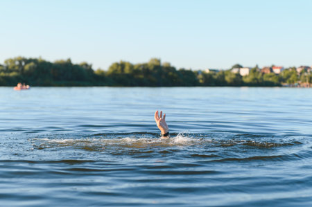 Hand of a drowning man reaching out from the water, desperately asking for help in a river during a...