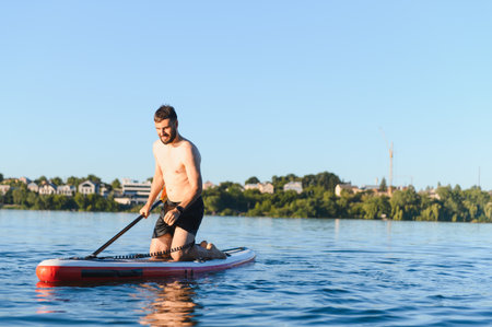 Young man paddling on a sup board on a lake on a summer afternoon, enjoying water sports and relaxingの写真素材