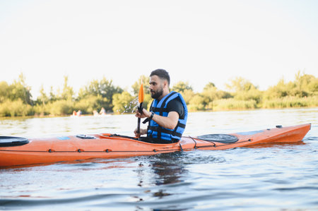 Man wearing life jacket paddling orange kayak on lake, enjoying water sports and active recreation...