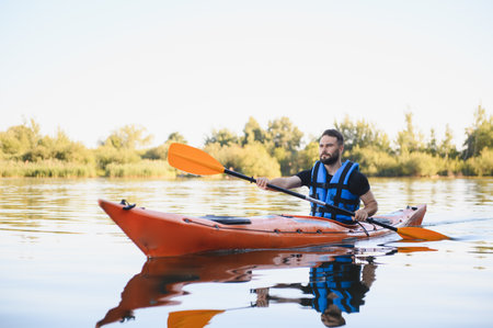 Young man kayaking on a lake surrounded by beautiful nature, enjoying water sports and active...