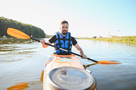 Man paddling a kayak on a river during a sunny summer day, enjoying active recreation and the thrill...