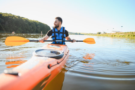 Man paddling orange kayak on calm water, enjoying active recreation and water sports on a summer day