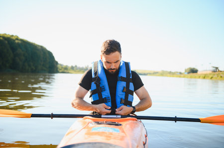 Man fastening his life vest while sitting in kayak on the river and getting ready for kayaking trip...