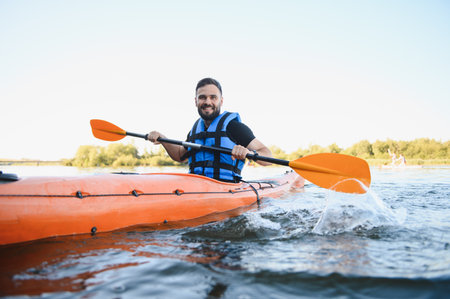 Man paddling orange kayak on river in sunny summer day, wearing life vest and enjoying water sport...