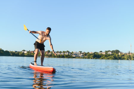 Young man paddling and maintaining balance on a stand up paddleboard while enjoying a beautiful...