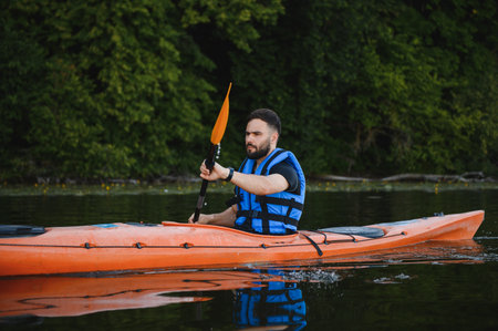 Man paddling orange kayak on calm lake water wearing life jacket enjoying active recreation and...