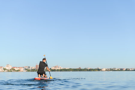 Man paddling on a sup board on a lake, enjoying a sunny day with a cityscape in the background