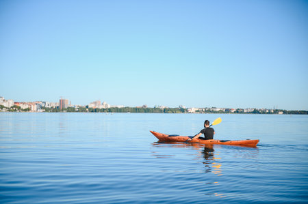 Man kayaking on a peaceful lake with a cityscape on the horizon, enjoying a sunny day of water...