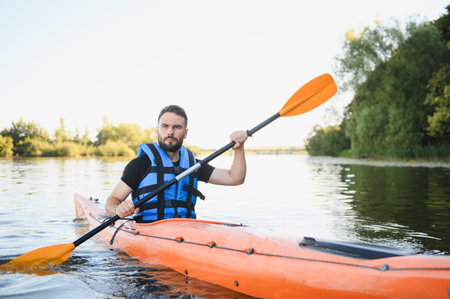 Kayaker wearing a life jacket paddles an orange kayak on a calm river, enjoying the summer day and...