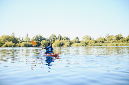 Man kayaking on a peaceful lake surrounded by lush vegetation, enjoying water sports and embracing...