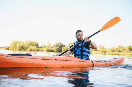 Man wearing life jacket paddling orange kayak on calm water enjoying active recreation and water...