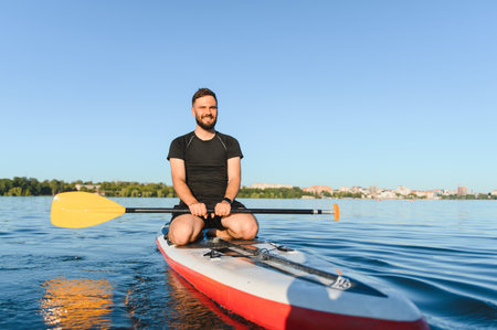 Young sportsman paddling on a stand up paddle board across a serene lake in the city, enjoying a...