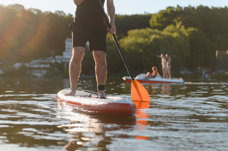Man is paddling on a sup board, enjoying a moment of active recreation on the lake during sunset