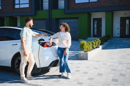 Couple chatting next to their electric car charging at their modern home, showing sustainable living and eco conscious choicesの写真素材