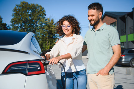 Happy couple charging their electric vehicle at home, demonstrating commitment to eco friendly transportation and sustainable livingの写真素材