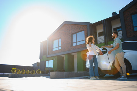 Couple chatting while charging their electric car outside their modern, eco friendly home, embracing sustainable living and green energyの写真素材