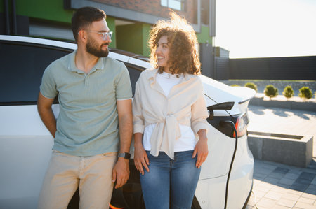 Happy couple smiling while charging their electric vehicle at their house, demonstrating commitment to eco friendly transportation and renewable energyの写真素材
