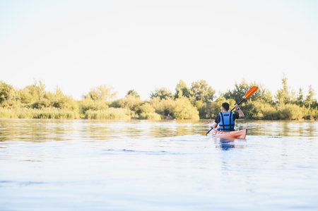 Man paddling a kayak on a calm lake, enjoying the serene water sport activity while surrounded by...