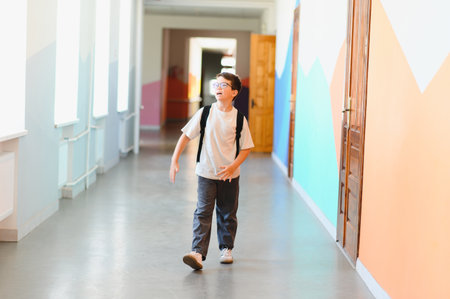 Elementary school student walking in school corridor during break time, wearing backpack and eyeglassesの写真素材