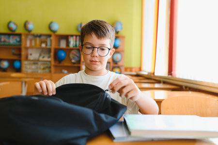 Young student opening his backpack at a school desk, getting ready for class and eager to learnの写真素材
