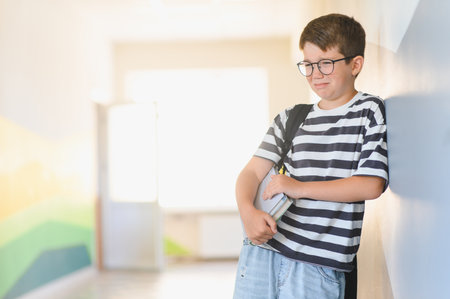 Sad schoolboy crying and holding books in the school hallway after suffering bullying from classmatesの写真素材