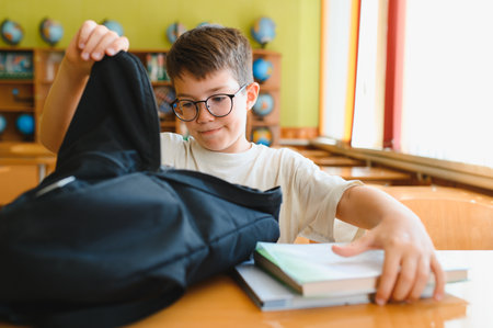 Young boy unpacking school backpack and books on desk in classroom, getting ready for learningの写真素材