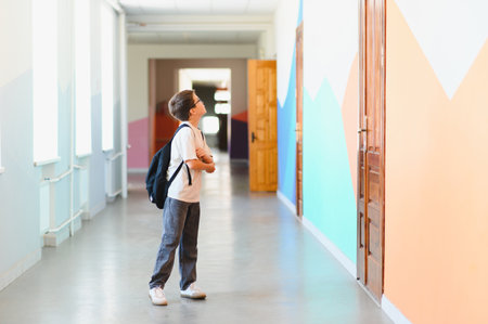 Elementary school student looking up with arms crossed in colorful school hallway, contemplating the new school yearの写真素材