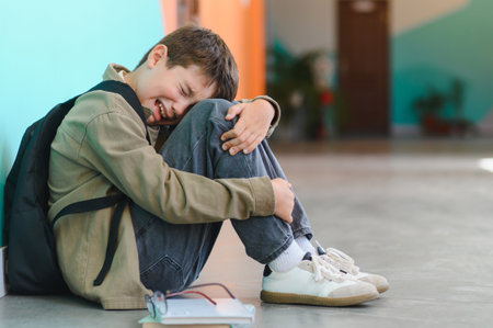 Sad schoolboy crying on the floor at school after suffering from bullying by classmates, concept of child abuseの写真素材