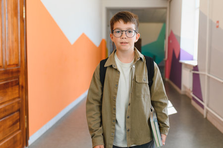 Elementary student walking in colorful school hallway carrying book and wearing backpack, ready for class and eager to learnの写真素材