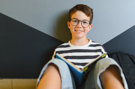 Happy young student wearing eyeglasses smiling while reading a book during break time at school