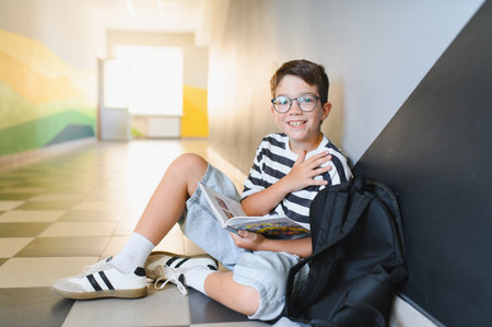 Happy young student reading a book while sitting on the floor in a school hallway, enjoying his break timeの写真素材