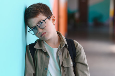 Sad schoolboy leaning against a wall in a school corridor, crying and feeling overwhelmed by bullying from classmates, experiencing deep emotional painの写真素材