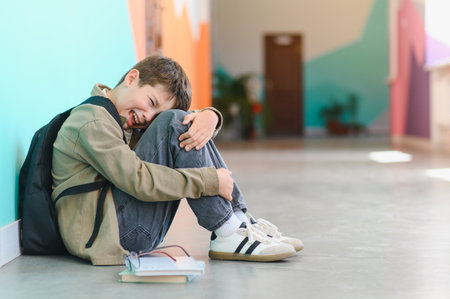 Sad schoolboy crying and hugging his knees, feeling the weight of bullying at school, experiencing deep loneliness and emotional painの写真素材