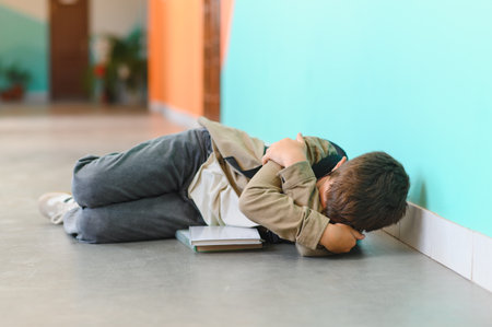 Sad schoolboy lying on the floor crying and hugging himself after suffering bullying at schoolの写真素材