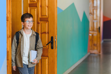 Happy boy with glasses and backpack entering school carrying books, ready for learning and studyingの写真素材