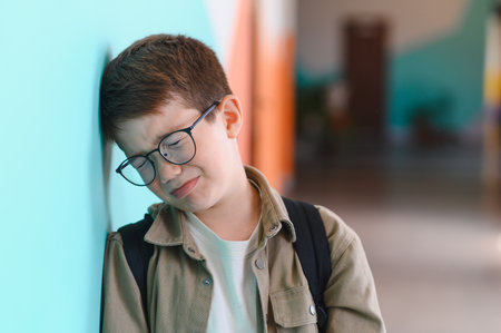 Sad schoolboy crying in the school corridor, feeling the weight of bullying and isolation from...
