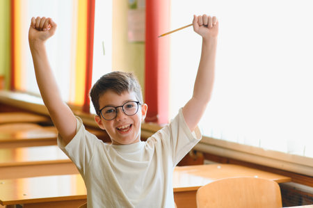 Happy student celebrating successful learning, raising hands with pencil in classroom, expressing...